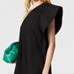 A woman wears the Stella McCartney Washed Cotton Asymmetric Mini Dress in black, holding a green clutch; her head and upper torso are shown against a plain background.