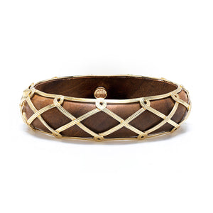 The Juliska Capucine De Wulf Earth Goddess Hinged Bangle is hand-carved from teak wood, adorned with a gold crisscross design and gold loop accents for a touch of elegance.