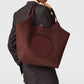 A person in a pinstripe suit holds the Stella McCartney Logo Reversible Suede Tote, featuring perforated “Stella McCartney” lettering.
