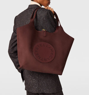 A person in a pinstripe suit holds the Stella McCartney Logo Reversible Suede Tote, featuring perforated “Stella McCartney” lettering.