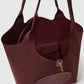 The Stella McCartney Logo Reversible Suede Tote is a spacious burgundy bag featuring a cutout logo, an open top, and an inner pocket with a snap closure.