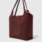 The Logo Reversible Suede Tote by Stella McCartney is crafted in burgundy suede, featuring double handles and a circular front patch with perforated “Stella McCartney” text.