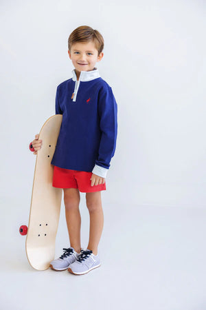 A young toddler smiles at the camera indoors, holding a skateboard and wearing The Beaufort Bonnet Company’s Baby Boys and Boys' Sheffield Shorts with an elastic waist, a blue pullover, and gray sneakers.