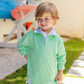 A young boy in The Beaufort Bonnet Company’s Baby Boys' and Boys' Prepletic™ Hayword Half Zip stands outside smiling, with colorful kayaks stacked in the background.