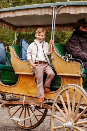 A young boy wearing The Beaufort Bonnet Company's Baby Boys' and Boys' Sherpa Van Camp Vest stands on a vintage horse-drawn carriage step, smiling at the camera, while an adult driver with a hat sits at the front.