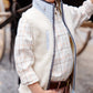 A young boy in The Beaufort Bonnet Company's Baby Boys' and Boys' Sherpa Van Camp Vest, layered over a plaid shirt and pink pants, stands outdoors with one hand in his pocket, smiling and looking to the side.