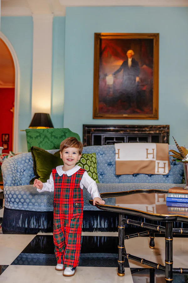 A smiling young child wears the Baby Boys' Lawson Longall by The Beaufort Bonnet Company, standing in a stylish living room with a blue sofa and a framed portrait on the wall.