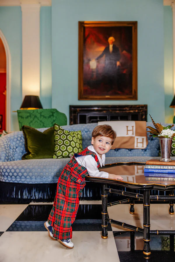A young boy in The Beaufort Bonnet Company’s Baby Boys' Lawson Longall leans on a coffee table in a stylish living room with blue walls, a patterned sofa, and a portrait above the fireplace.