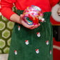 Wearing The Beaufort Bonnet Company's Girls' Critter Beasley Bag Skirt, this person holds a colorful Christmas ornament.