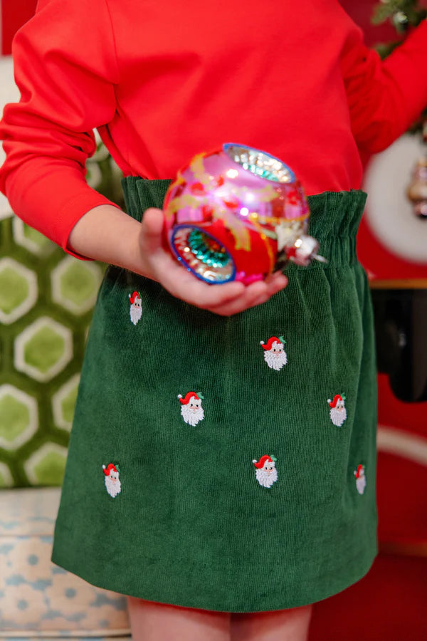 Wearing The Beaufort Bonnet Company's Girls' Critter Beasley Bag Skirt, this person holds a colorful Christmas ornament.