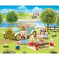 Calico Critters toy animal figures enjoy a picnic beside the Classic Family Car on grass near a river, with trees, a fence, and a house in the background under a blue sky. The scene features charming accessories for the Classic Family Car, including seating for up to 10 figures, making it perfect for imaginative play.
