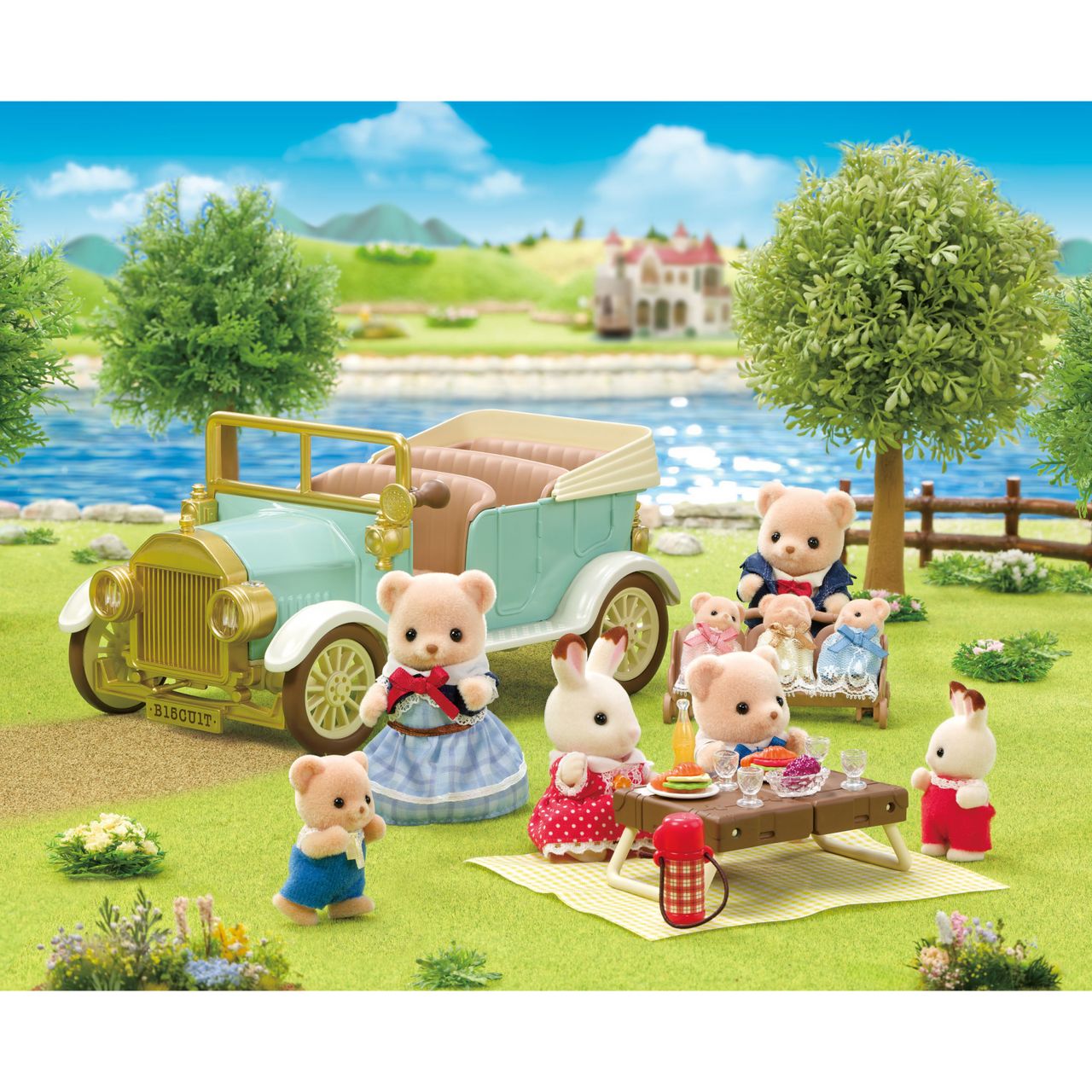 Calico Critters toy animal figures enjoy a picnic beside the Classic Family Car on grass near a river, with trees, a fence, and a house in the background under a blue sky. The scene features charming accessories for the Classic Family Car, including seating for up to 10 figures, making it perfect for imaginative play.