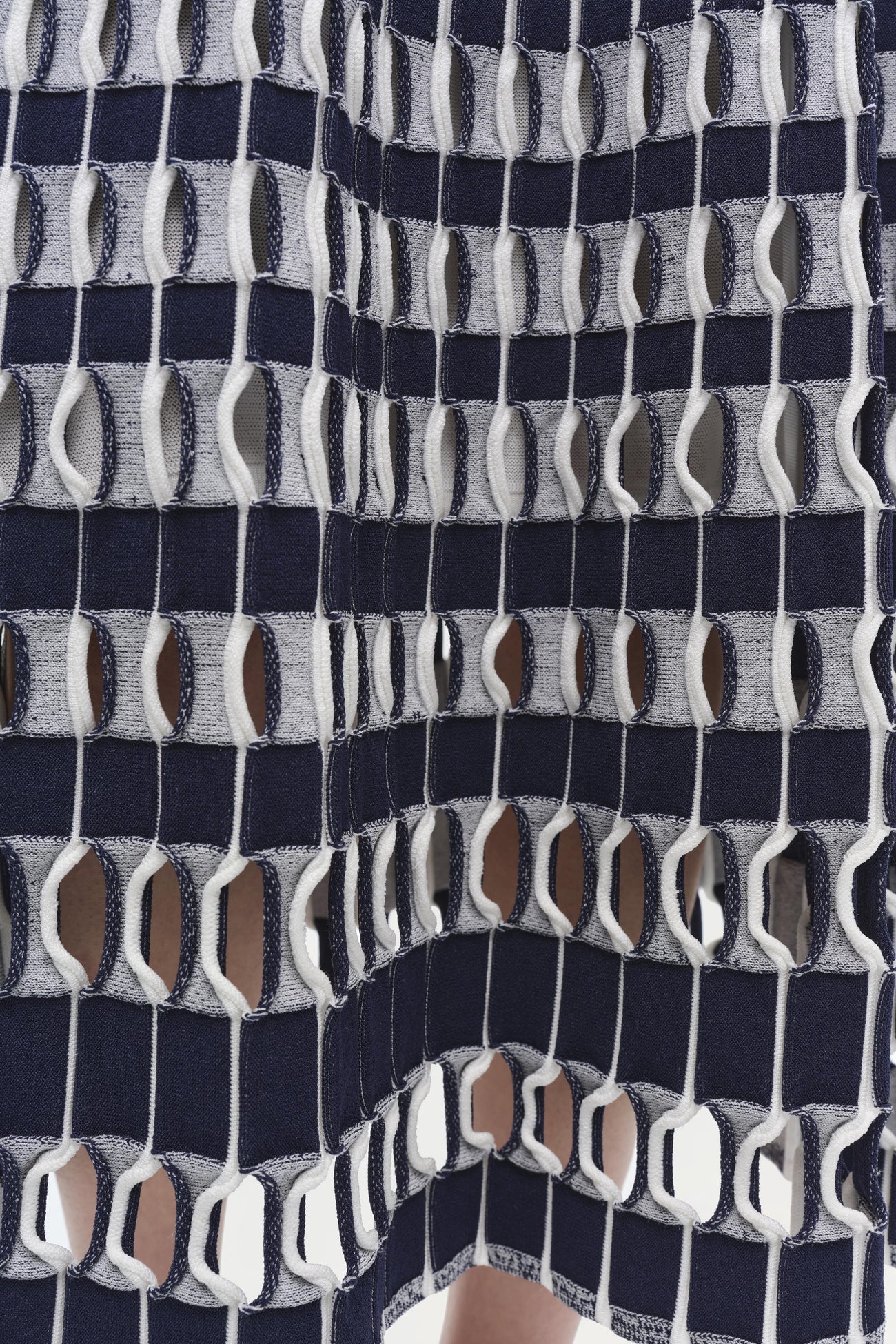 Close-up of the Simkhai Larken Midi Skirt featuring a navy and white textile pattern with interlocking loops, forming a net-like grid reminiscent of bold gingham knitwear.