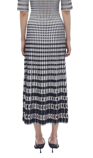 A person wearing the Simkhai Larken Midi Skirt, featuring a bold black and white pattern, paired with black strappy heels, seen from the back.