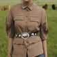 A person stands in a grassy field wearing the Lela Rose Melange Crepe Camp Shirt, which features a classic silhouette. They have paired it with jeans and a large belt adorned with silver details, while cows graze in the background.