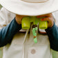 A child dressed in the Great Pretenders Forest Guardian Set with Accessories, including a cream safari costume and hat, holds green toy binoculars up to their face, covering their eyes.