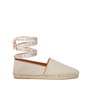 The Gaia Canvas Flat by Stella McCartney is a lightweight beige espadrille featuring a textured canvas upper, woven sole, and branded ankle strap.