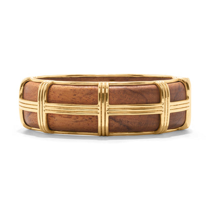 The Gaia Hinged Bangle by Juliska Capucine De Wulf features hand-carved wide teak wood adorned with raised gold accents in a rectangular grid pattern, where gold bands intersect elegantly across the surface.