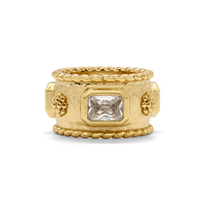 The Berry Band Ring by Juliska Capucine De Wulf features a wide hammered gold band, a central rectangular clear gemstone, intricate rope edging, crystal accents, and delicate floral details along the band.