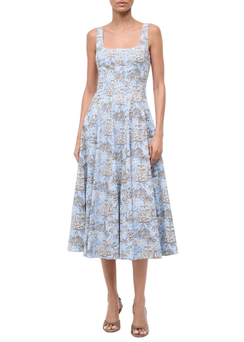 A woman wearing the Staud Wells Dress in Sky Toile, a sleeveless, light blue floral midi dress with a fitted waist and square neckline, paired with brown open-toe heels.