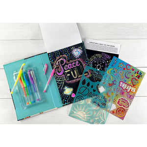 The Sparkling Aspirations Art Journal by Bright Stripes is arranged on a white surface, featuring neon gel pens, scratch sheets with "Peace" and "Dreams" designs, a plastic stencil, drawing paper, and a booklet.
