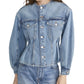 A woman wears the Frame Nipped Collarless Jacket in light blue cotton denim with front buttons, paired with matching jeans, photographed from mid-thigh up.