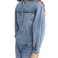 A person with long brown hair models Frame's The Nipped Collarless Jacket, paired with matching denim jeans, standing against a white background.