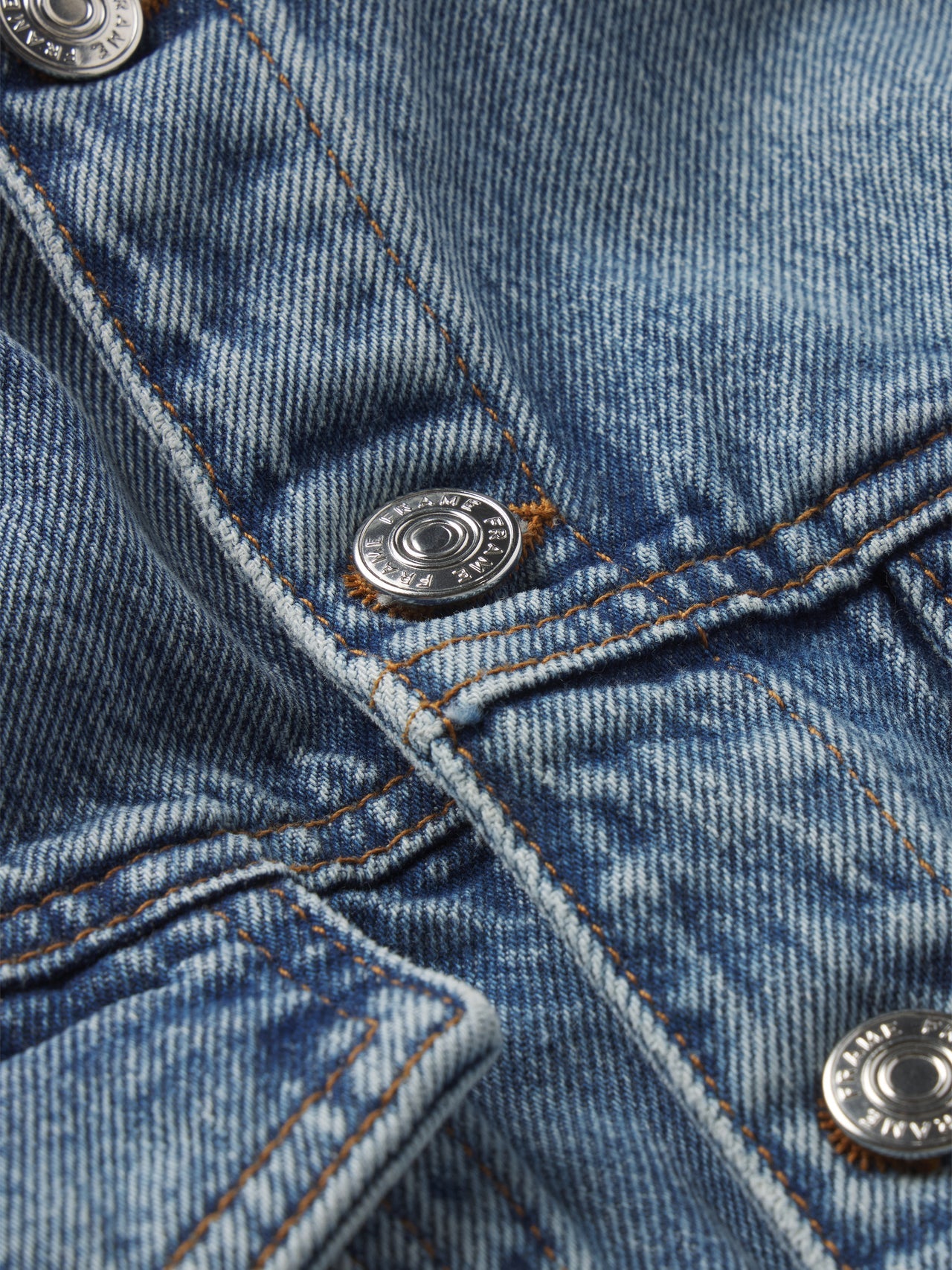 Close-up of The Nipped Collarless Jacket by Frame, featuring blue cotton denim, orange stitching, and metal snap buttons.