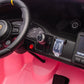 Close-up of the Freddo 24V Porsche 911 GT3 Pink 2 Seater Ride-On’s dashboard, featuring a steering wheel, push-button start, red button, gauge, plastic keys, and part of a touchscreen display. Bright pink accents highlight the floor and dashboard. This detail-rich interior brings the thrilling luxury of a real Porsche to every drive.