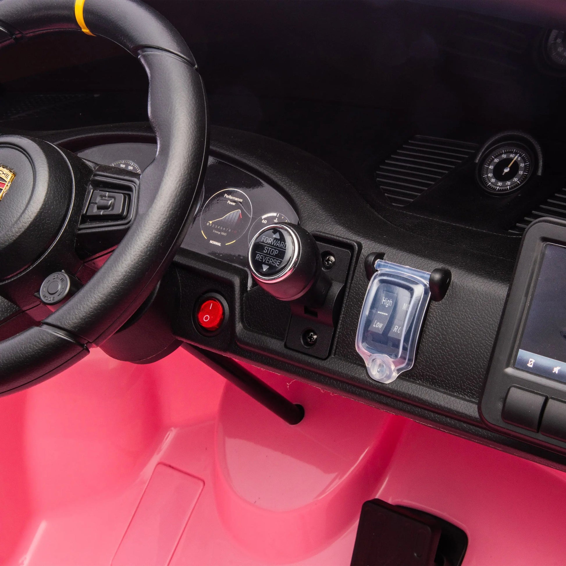 Close-up of the Freddo 24V Porsche 911 GT3 Pink 2 Seater Ride-On’s dashboard, featuring a steering wheel, push-button start, red button, gauge, plastic keys, and part of a touchscreen display. Bright pink accents highlight the floor and dashboard. This detail-rich interior brings the thrilling luxury of a real Porsche to every drive.