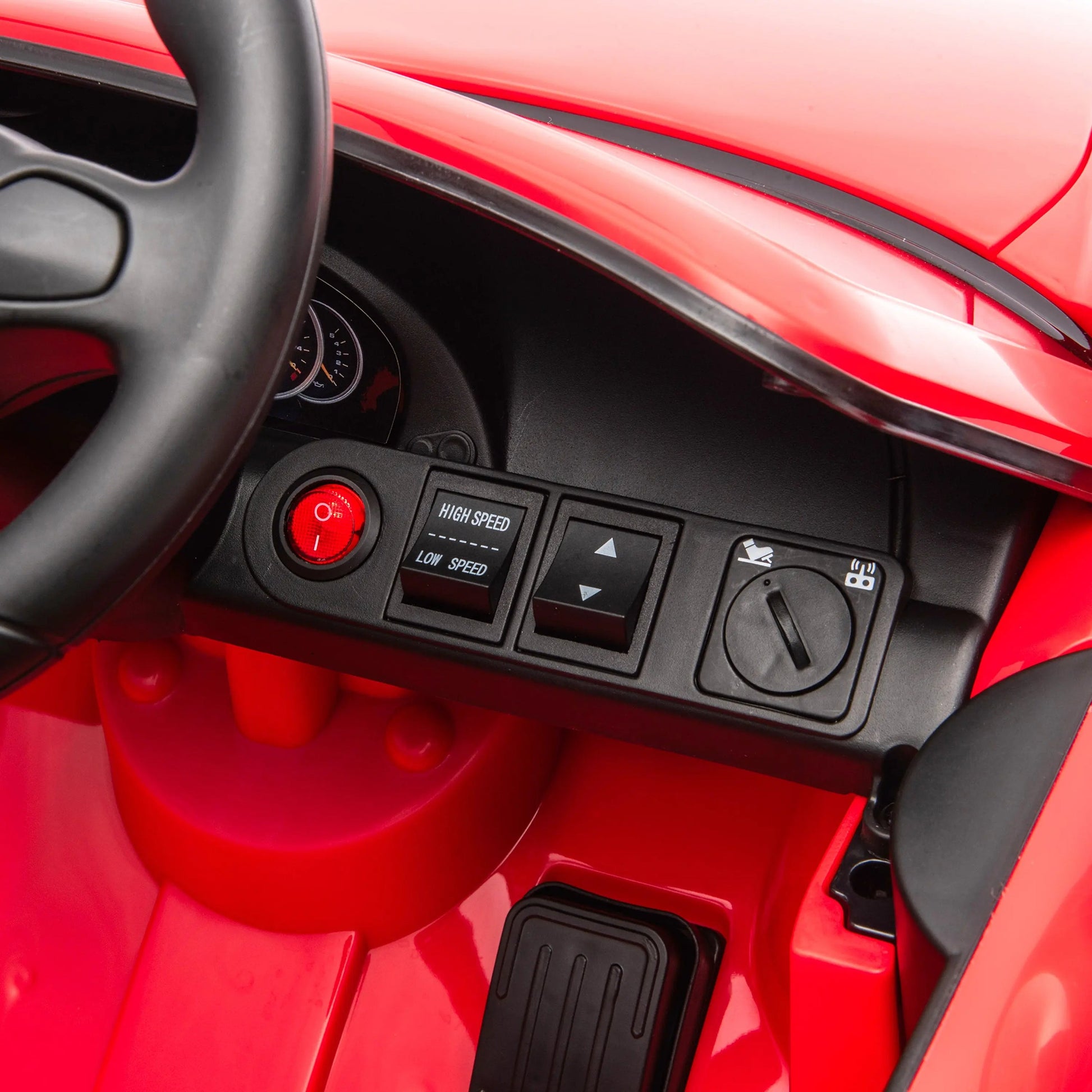 Close-up of the Freddo 12V Porsche Carrera GT 1 Seater Ride-On dashboard featuring a steering wheel, speed control buttons, arrow buttons, a power button, an ignition switch, and a visible foot pedal below in this motorized vehicle.