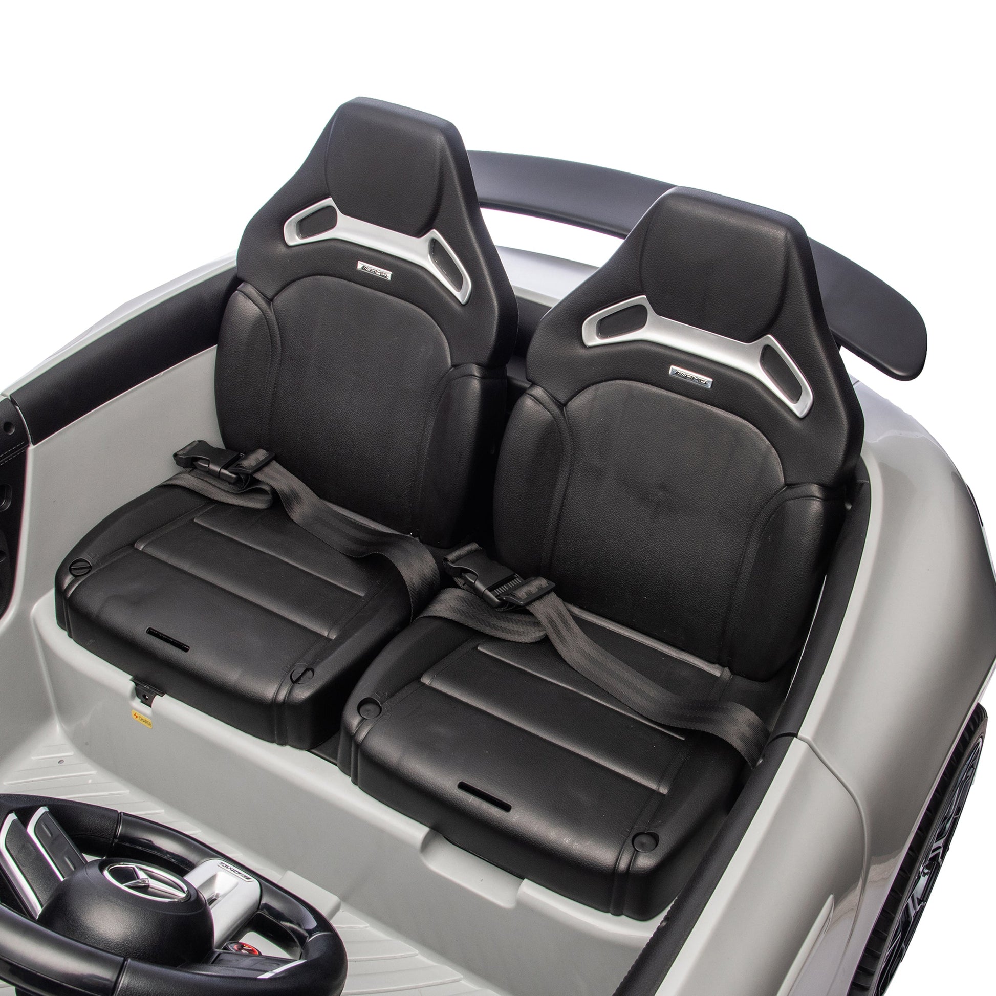 Two black seats equipped with seat belts are visible from above inside the Freddo 24V Mercedes AMG GT63 Gray 2 Seater Ride-On. The interior features a light gray design, and part of the steering wheel appears in the lower left corner of this stylish ride-on car.