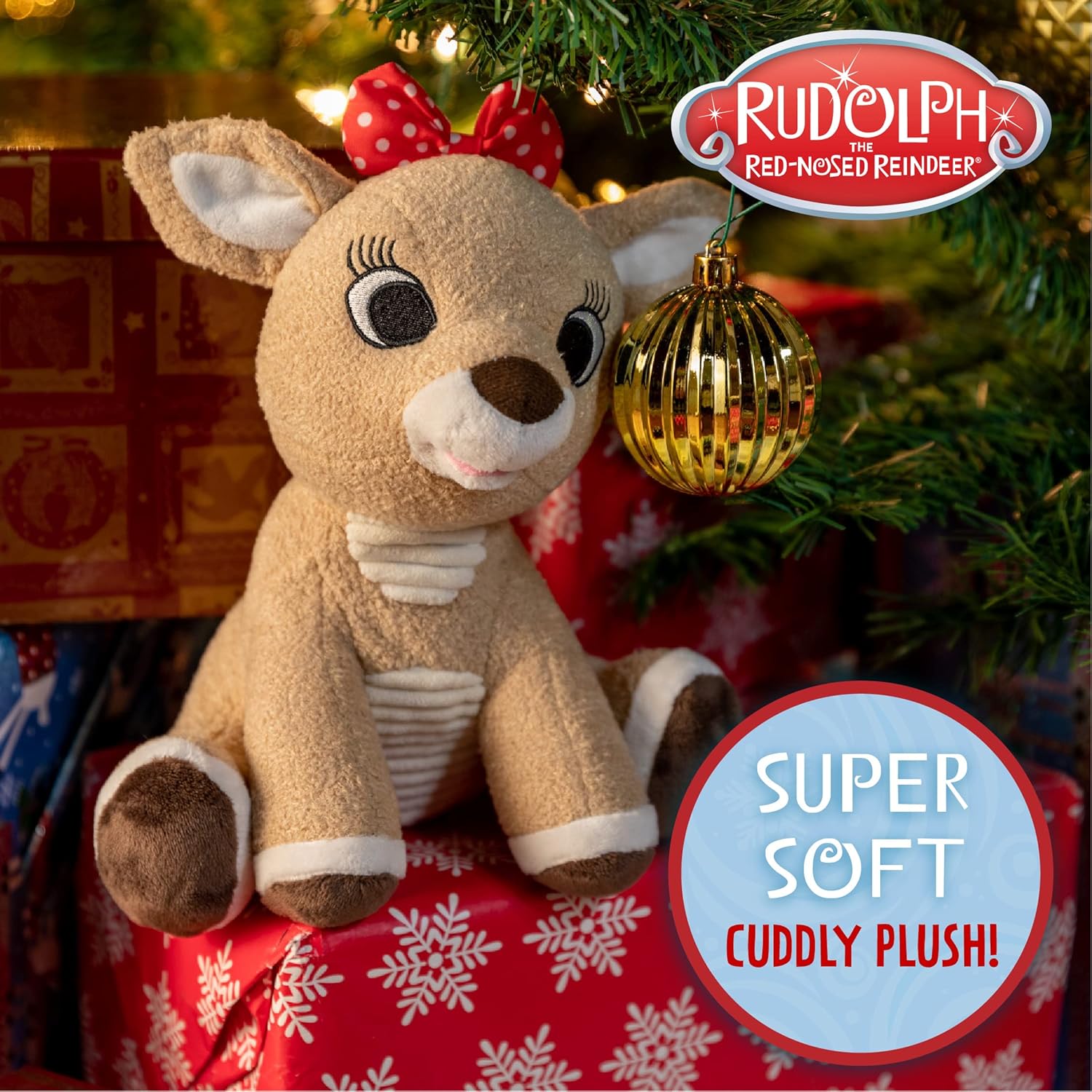 A plush Clarice reindeer toy with a red bow sits on wrapped gifts under an ornamented Christmas tree. Text reads, "Clarice," "Kids Preferred," and "Super Soft Cuddly Plush!"—a true Christmas classic.