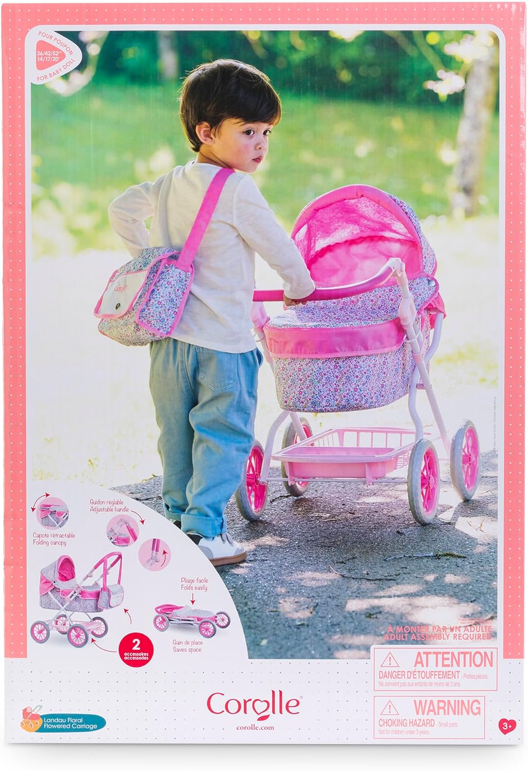 A young child stands outside, holding the handle of the Corolle Carriage - Bright Pink Floral stroller with a matching shoulder bag. The packaging displays safety warnings and features a height-adjustable handlebar.