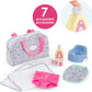 The Corolle Floral Changing Accessories Set includes 7 doll accessories: a floral bag with pink handles, blue potty, bottle, pump tube, bib, diaper, and cloth. A close-up shows a hand pressing the pump bottle.