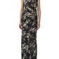 A woman wears the Simkhai Acacia Jersey Midi Dress—a sleeveless, ankle-length dark floral printed dress with a ruched side detail—paired with black sandals, standing against a plain white background.