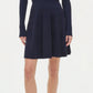 A woman wears the Simkhai Alcott Knit Mini Dress—a navy blue, ribbed knit mini with a spread collar, long sleeves, and flared skirt—paired with black open-toe heeled sandals.