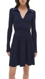 A woman wearing the Simkhai Alcott Knit Mini Dress—a navy blue, long-sleeve mini dress with a ribbed knit fabric, flared skirt, and V-neckline.
