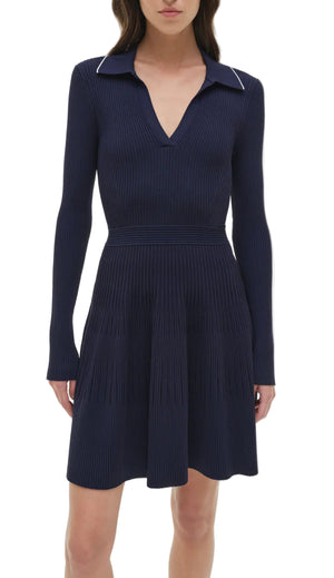 A woman wearing the Simkhai Alcott Knit Mini Dress—a navy blue, long-sleeve mini dress with a ribbed knit fabric, flared skirt, and V-neckline.