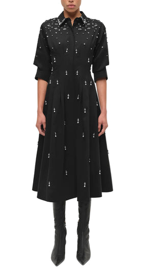 A person wearing the Simkhai Jazz Embellished Midi Dress—black cotton poplin with an A-line skirt and crystal pearl details—paired with black knee-high boots.
