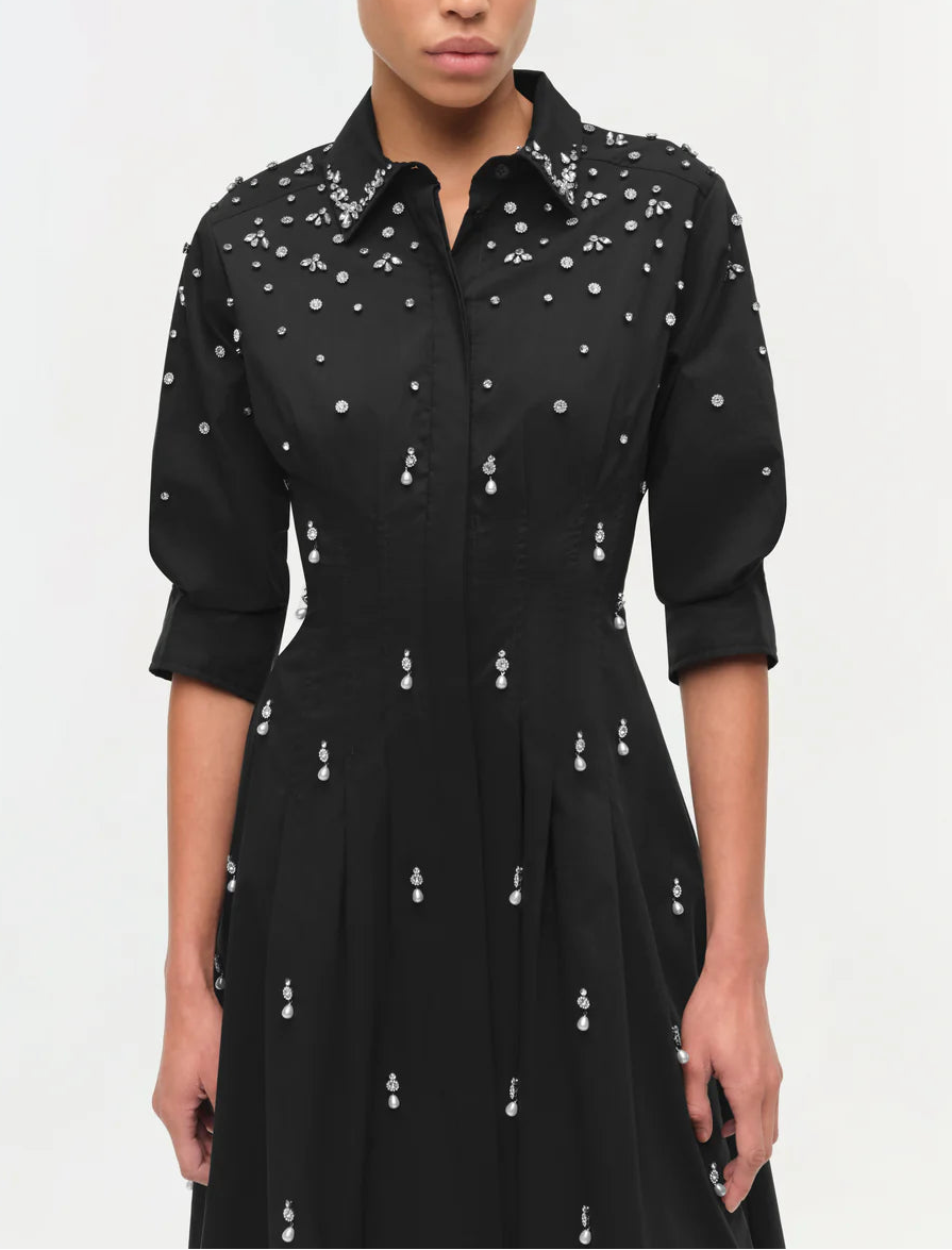 A person wearing the Simkhai Jazz Embellished Midi Dress, a black cotton poplin midi with three-quarter sleeves, an A-line skirt, and scattered silver bead accents.