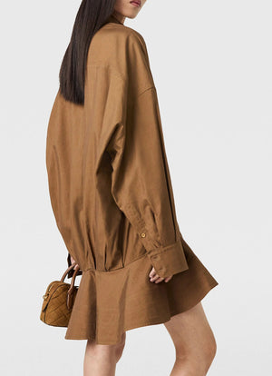 A person with long dark hair wears the Stella McCartney Washed Cotton Peplum Shirt Dress and carries a small brown quilted handbag.