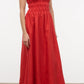 A woman stands on a plain floor in flip-flops, wearing the Staud Ayla Linen Dress—a sleeveless, ankle-length red dress with thin straps and a gathered waist.