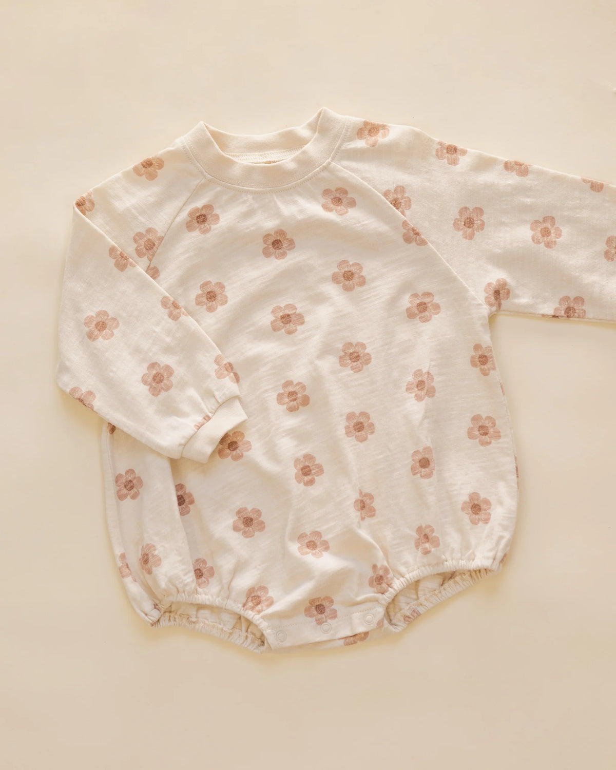 Rylee & Cru Baby Girls’ Crew Neck Romper, made from soft jersey fabric in a cream color with a pink flower pattern, features long sleeves and elastic leg openings and is shown laid flat on a neutral background.