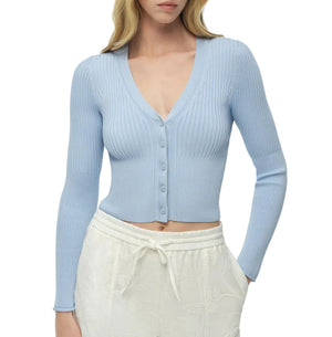 A woman wearing the Simkhai Ailany Cardigan, a light blue ribbed knit button-front cropped cardigan, paired with white drawstring pants.