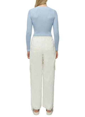 A person wearing the light blue, ribbed knit Ailany Cardigan by Simkhai and loose white pants stands facing away from the camera.