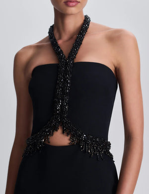 Simkhai Zoriel Gown in black, featuring a strapless column silhouette, an embellished halter neckline, and a beaded cutout detail at the midriff.