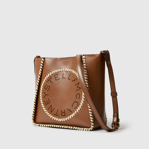 The Stella McCartney Logo Raffia Trim Crossbody Bag features brown vegan leather, a circular front logo cutout, and cream raffia trim along the edges.