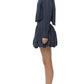 A woman stands in profile against a white background, wearing Simkhai's navy blue cotton poplin Pippa Bubble Mini Skirt, a matching long-sleeve shirt, and white open-toe heels.