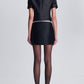 Rear view of a person wearing a structured Simkhai Naelle Top with white trim and a matching black mini skirt, styled with sheer black tights and black heels.